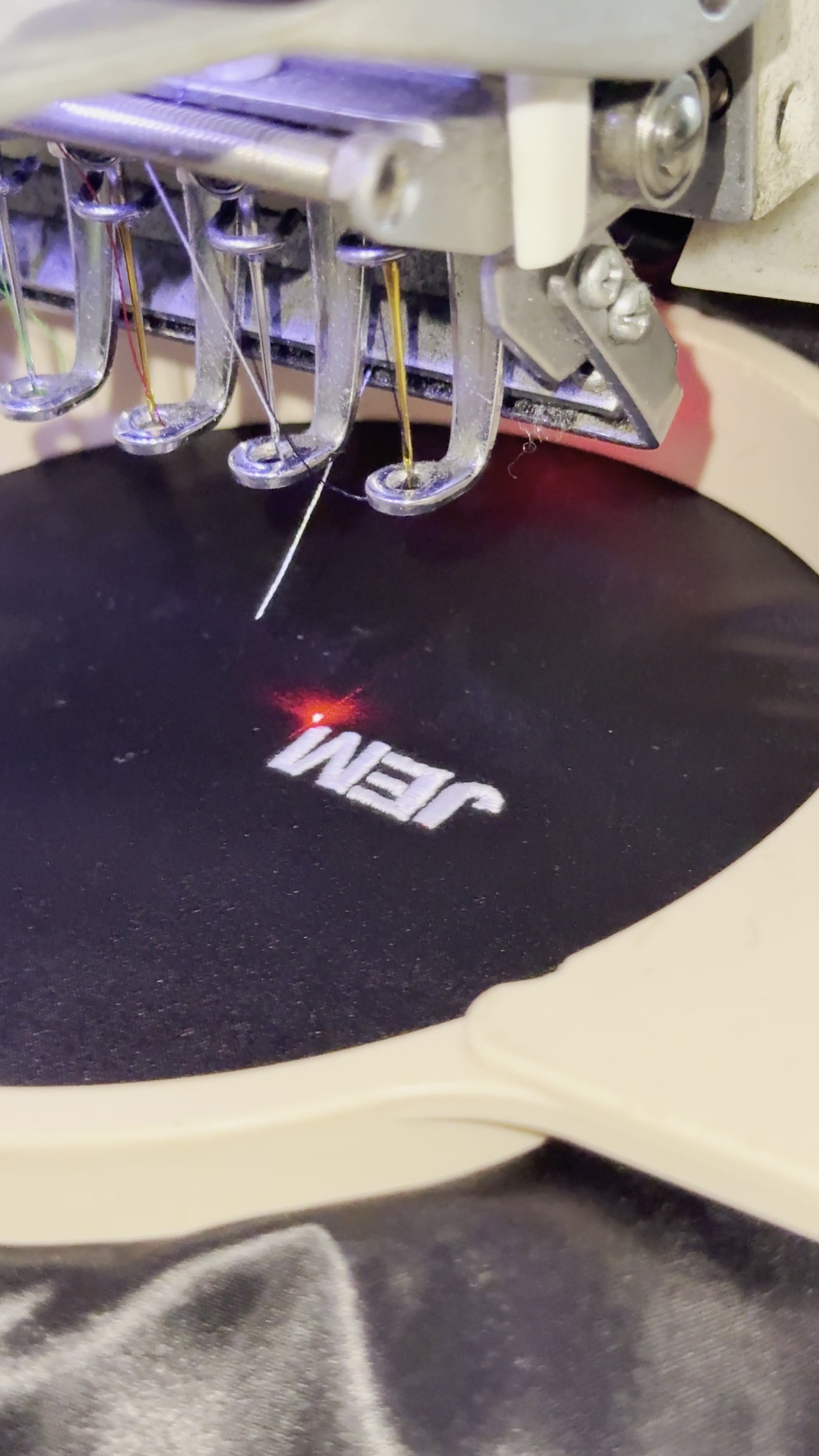 Commercial embroidery machine needles stitching a white logo onto black fabric in the hoop
